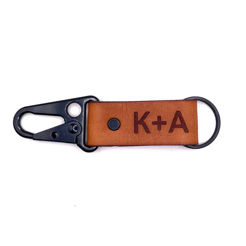 Leather keychain with initials 'K' and black carabineer, attached to a wooden accent.